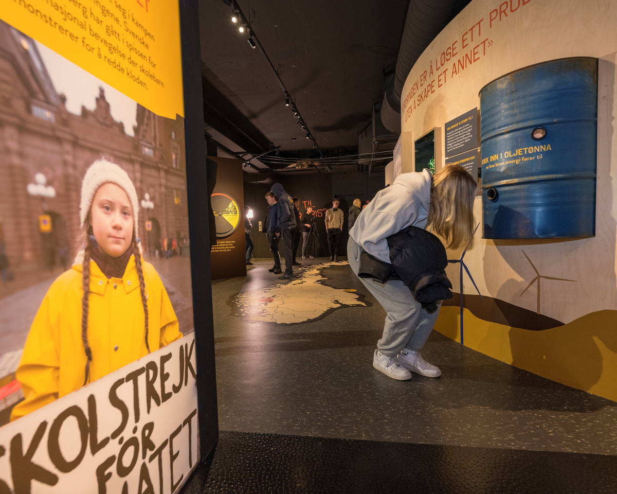 Elevbesøk i utstillingen «Kraft til enhver pris» på Norsk skogmuseum i Elverum. Fotografiet er tatt ved inngangen til denne tematustillingen, som har et stort, bakbelyst lystbilde av den unge svenske miljøaktivisten Greta Thunberg (til venstre i forgrunnen) som blikkfang. Til høyre er vi ei jente som følger oppfordringen «Kikk inn i oljetønna. Se hva brun energi fører til». Det dreier seg om et blålakkert oljefat som har tre kikkhull. Der vil man finne bilder av oljebrukens skyggesider. I bakgrunnen skimter vi flere elever ved montasjer som har et kritisk blikk også på andre energikilder.
Utstillingen «Kraft til enhver pris» ble åpnet i februar 2022.