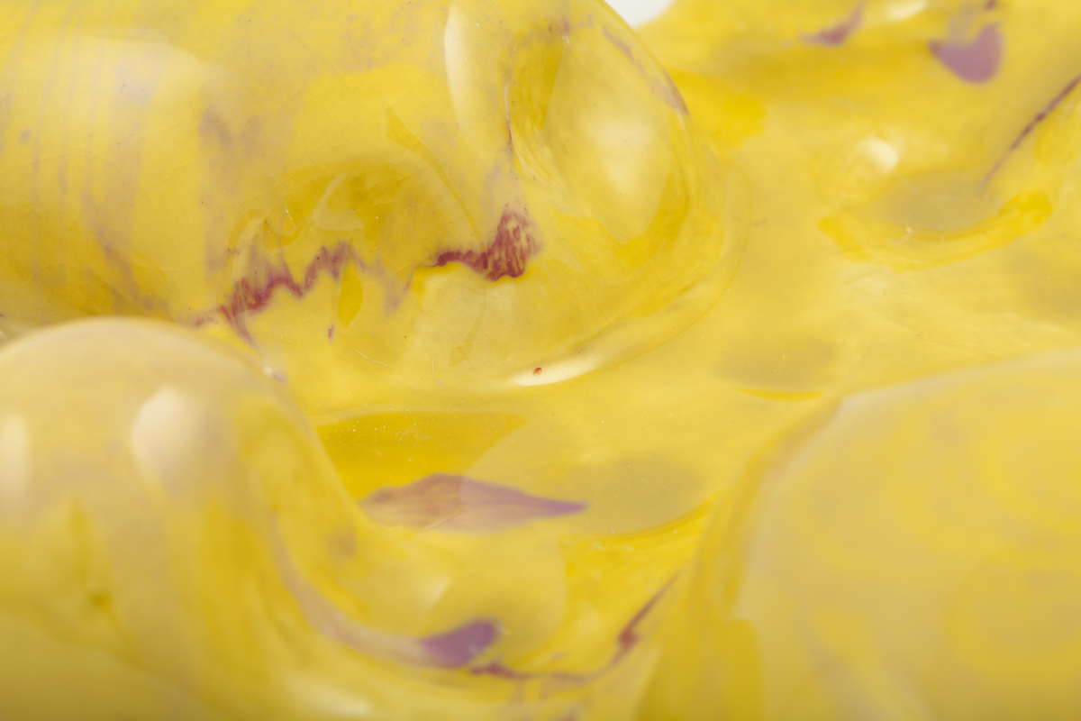 Keramisk objekt. Lav relieff-aktig form i gul og rosa. Den gule delen er i runde former med slett overflate. Den rosa delen ligger over og inni, og har mange små og spisse nupper. Undersiden er dekket av filt.