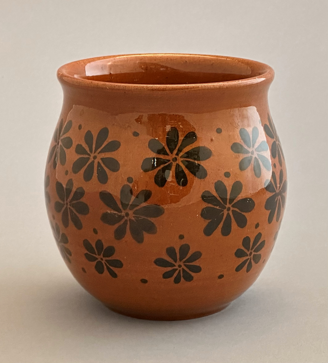 Rödbrun vas med svarta blommor av lergods.