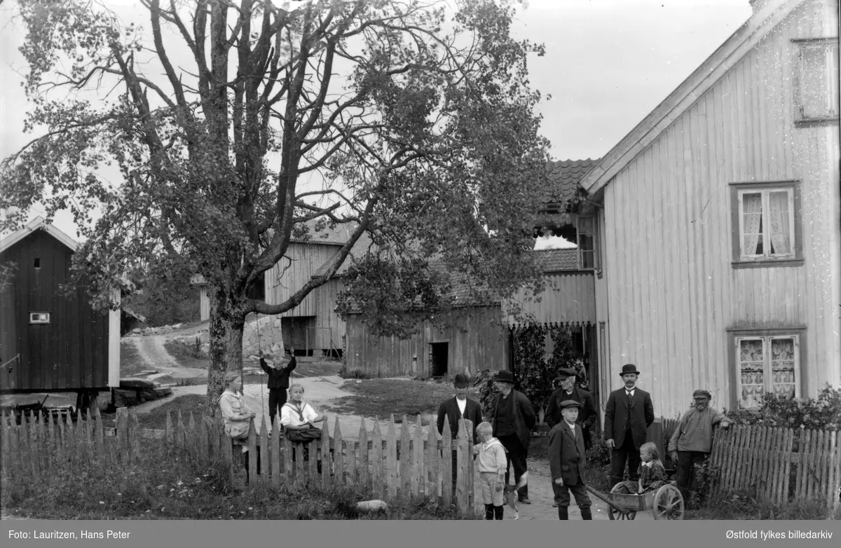 Menn og barn utenfor gården Sletta i Vestby en gang mellom 1910-1930.
Barna er kledd i matrosdress/kjole og mennene i hvit snipp.
En gutt med sixpence holder tretrille med pike oppi, en gutt husker i bakgrunnen. 
Se også nummer: ØFB. 2003-132