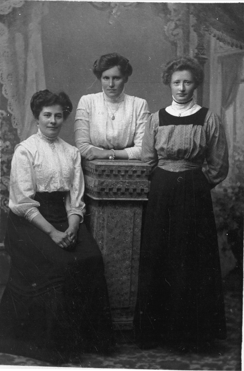 Studioportrett av tre kvinner, en sitter og to står.