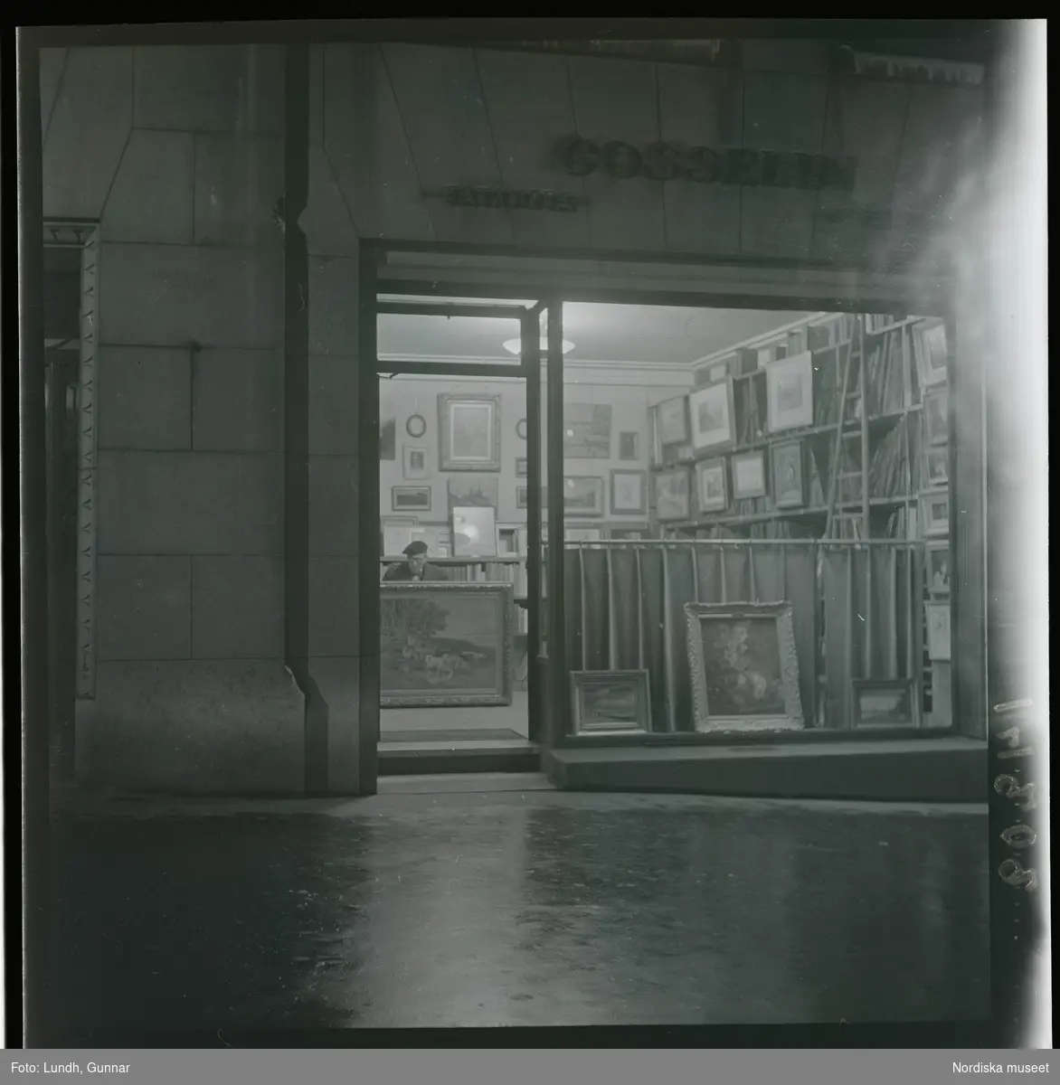 1950. Paris. En man sittter inne i en butik med konst, kväll