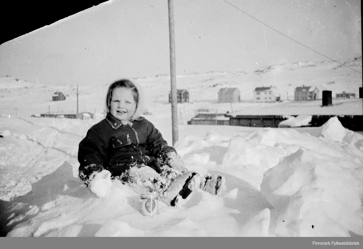 Havøysund 1952. Randi Bjørnstad sitter i snøen. "Hermetiske jordbær" boks ligger på bakken i forgrunnen.