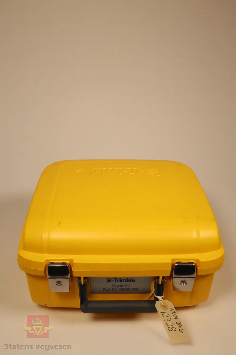 En gul koffert som inneholder en elektronsikemåleboken fra Trimble, et etui til måleboken og en Ethernet til 4-pin hun kabel. Det mangler ladekabel. Kofferten er ikke den som originalt kom med den elektronsikemåleboken men er av samme type som den som batteriladeren NVM 00-G-10307 kom med. 