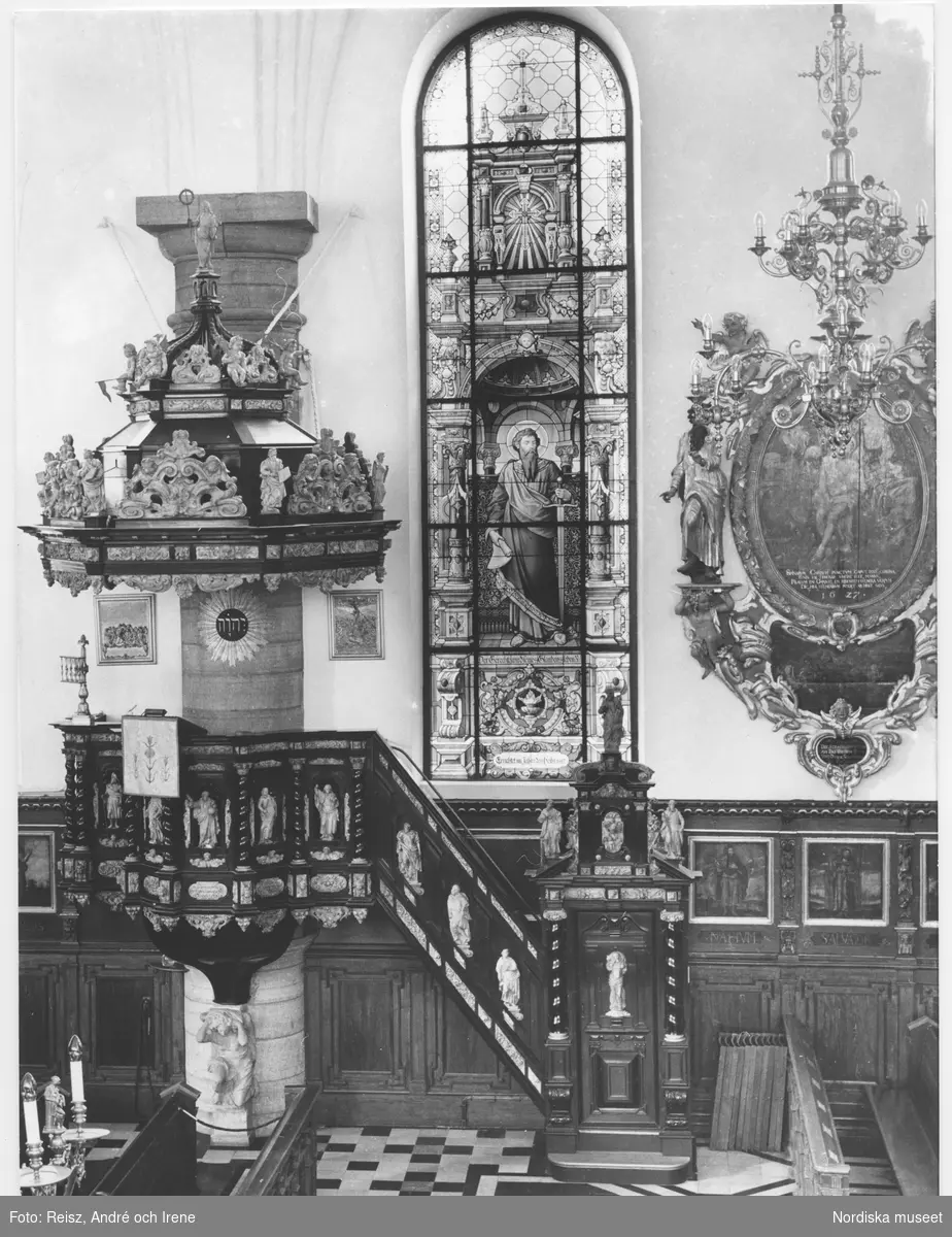Stockholm. Interiör från Tyska kyrkan byggd 1642 av byggmästaren Hans Jakob Kristler från Strasbourg. 
Predikstolen är tillverkad 1660 av ebenholts och alabaster. En knäböjande änglafigur av sten bär upp korgen, ljudtaket har en kupolliknande form smyckad med skulpturer och ornament. 
Glasmålningarna uppsatta mellan 1878 och 1911  är tillverkade av firman F. Zettler i München.