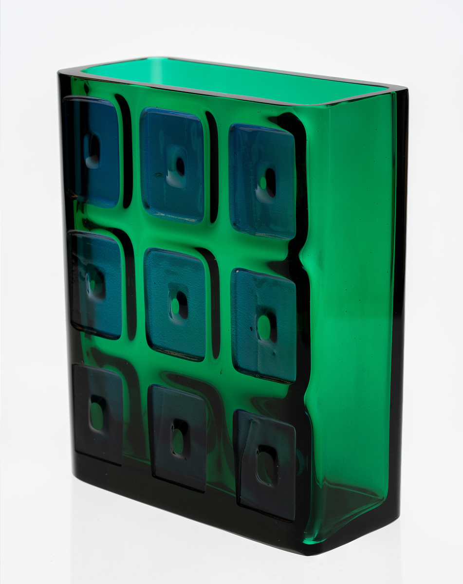 Rektangulær vase i grønnfarget gjennomskinnelig glass. Den ene langsiden er dekorert med ni blåfargede firkanter i relieff.