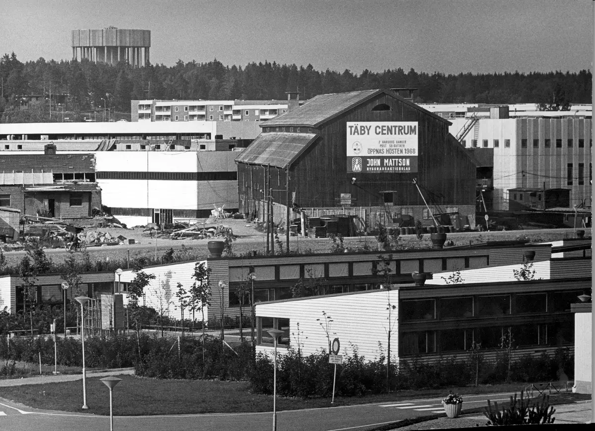 Under uppbyggnad av Täby Centrum användes Tibble gårds lada som magasin. Gammalt och nytt möts.
Vattentornet i Ensta i bakgrunden