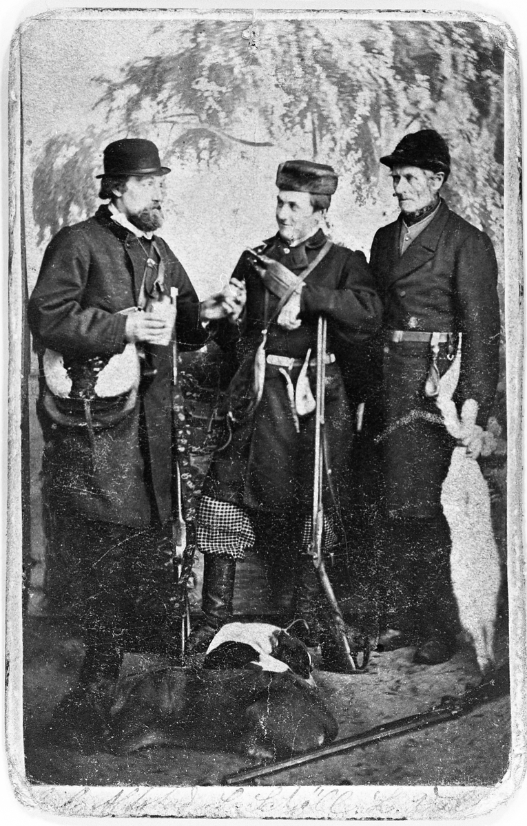 Tre harejegere med hund og bytte. Jegerne er Nils Alstad, L. Schjøll, og L. Walle, og året ca. 1870.