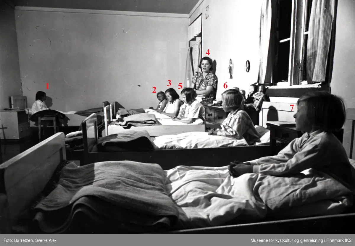 Skoleinternatet i Repvåg. Aftenbønn på jentenes sovesal. Husmor Judith Andreassen i bakgrunnen. Høsten 1952.