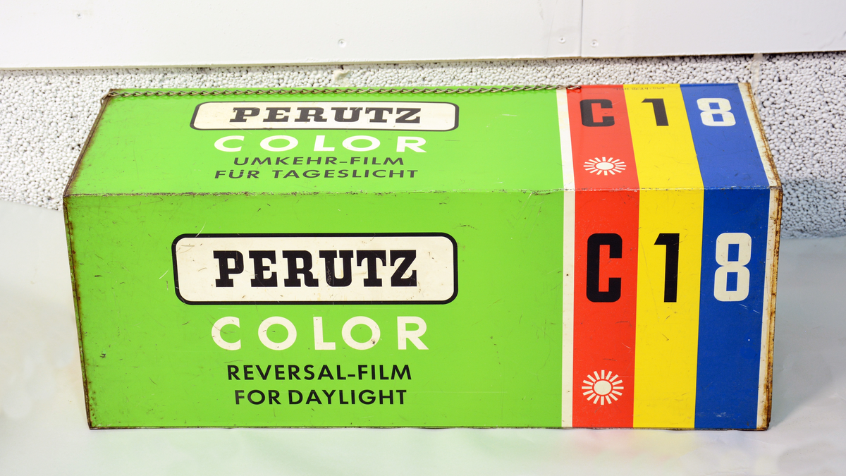 Reklame for Perutz Color C18, formet som en stor filmboks i metall med oppheng, til å henge opp på utsiden av fotobutikken.