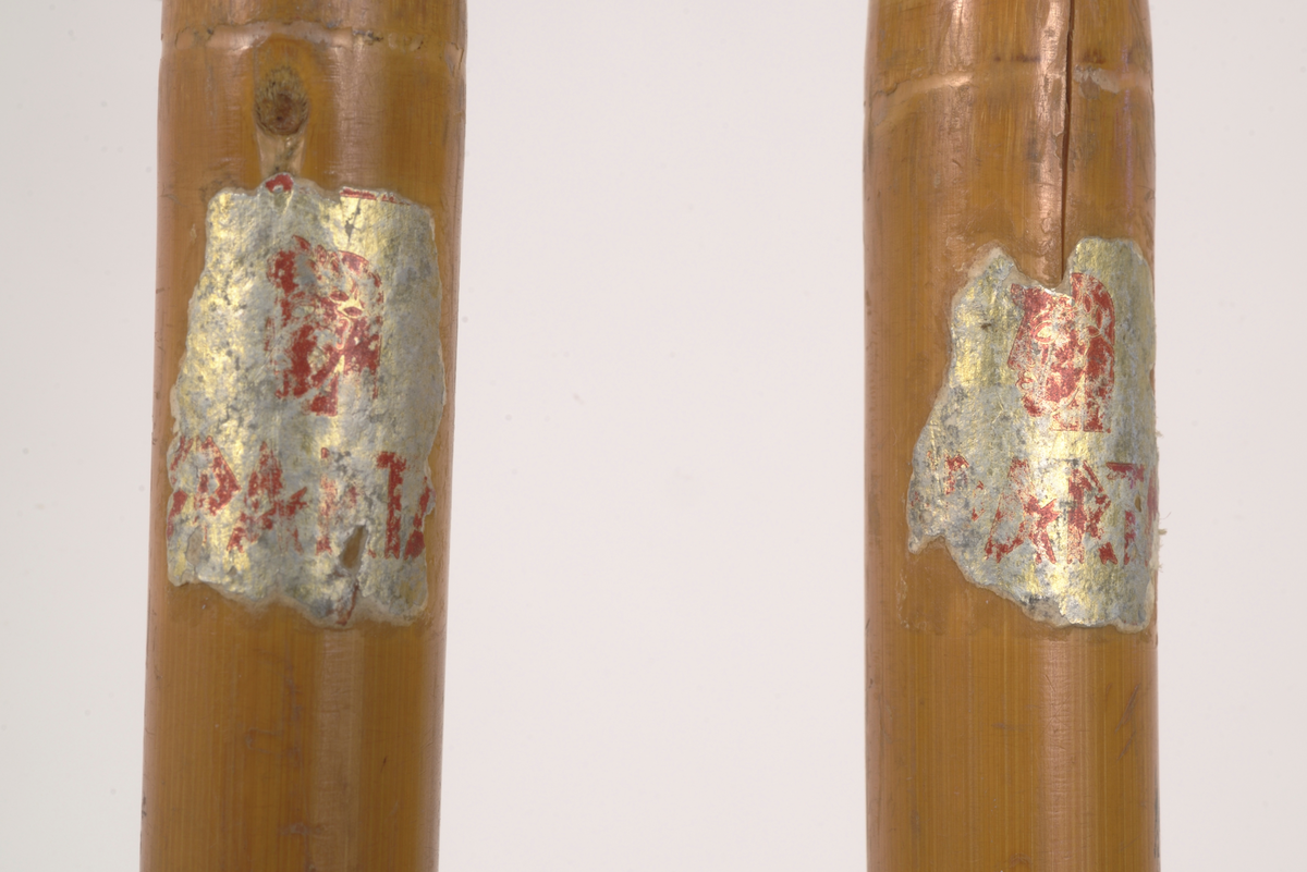 En av to skistaver, den andre A.06019-03.b. Selve staven er brun bambus. Håndtak, reimer og feste til trinse hvitt skinn. Metallpigg på enden. Trinsen av tre.