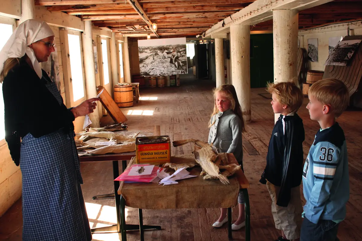 En kvinne kledd ut som klippfiskkjerring forteller tre barn om klippfisk inne i museet