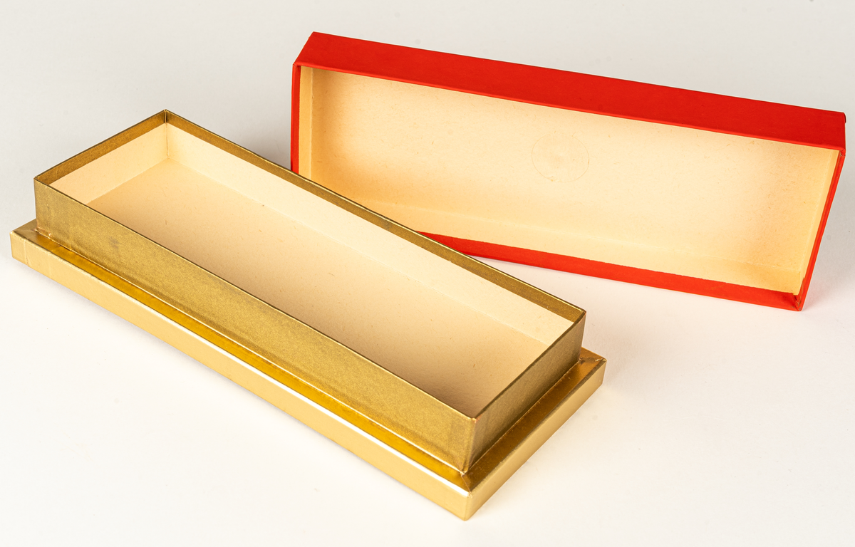 Ask i papp, rött lock, guldfärgad ask, avlång med liten guldfärgad knopp upptill.