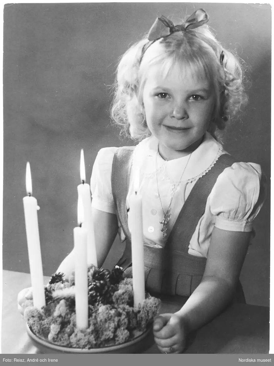 Jul. Porträtt av en flicka vid ett bord med en adventsjulstake med brinnande ljus.