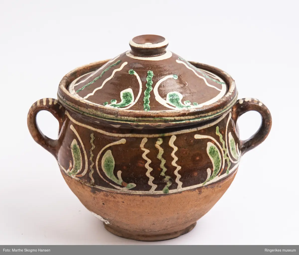 Keramikkrukke med lokk og to håndtak med gul og grønn dekor. Antagelig laget ved Hønefoss pottemakeri (1720-1850).