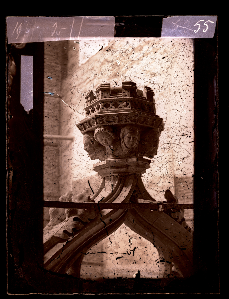 Kapitel på toppen av korbueveggen i oktogonen i Nidarosdomen. Dekorert med åtte hoder. Konsoll for Kristusfigur. 
Bildet skal i følge Hovedkatalog for fotografier være tatt før restaurering. Korbueveggen ble restaurert i perioden 1871-1872.