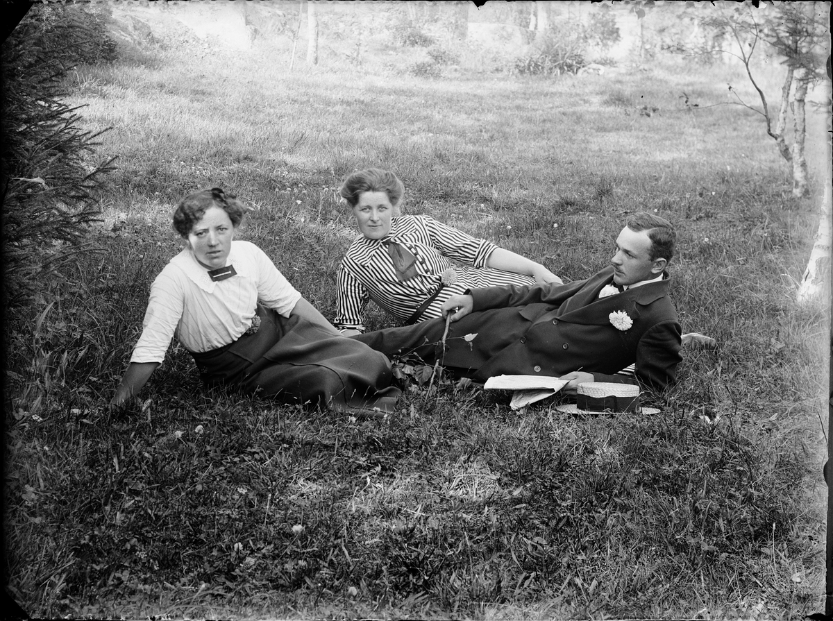 Man och två kvinnor i trädgård, sittandes i gräset, Alunda, Uppland