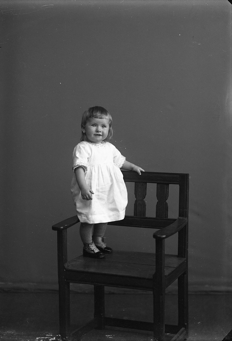Porträtt av en liten flicka som står på en stol.