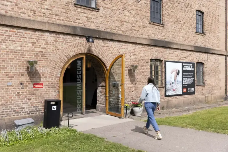 Kvinne går mot en åpen dør med teksten "Preus museum"