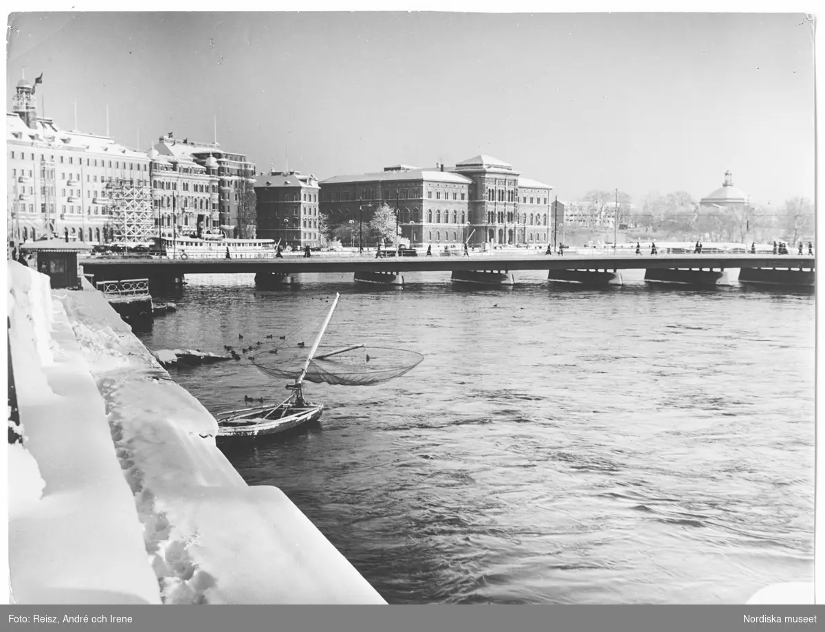 Utsikt över Stockholm bl a Nationalmuseum och Grand Hotel med snöklädda kajer i förgrunden.