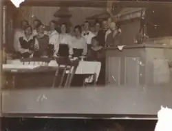 Kvinner står rundt et bord på et skolekjøkken. På baksiden a
