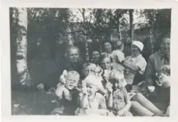 En gruppe barn og kvinner sitter på gresset i skogen, bildet