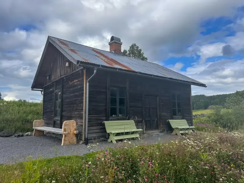 Iversmia i sol. To grønne utekrakker står på hver sin side av inngangen.