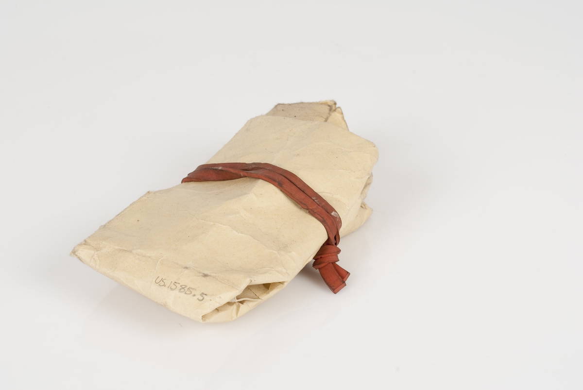 Maljer av metall i en papirpose med rød strikk over.
Maljene er i fargen brun.