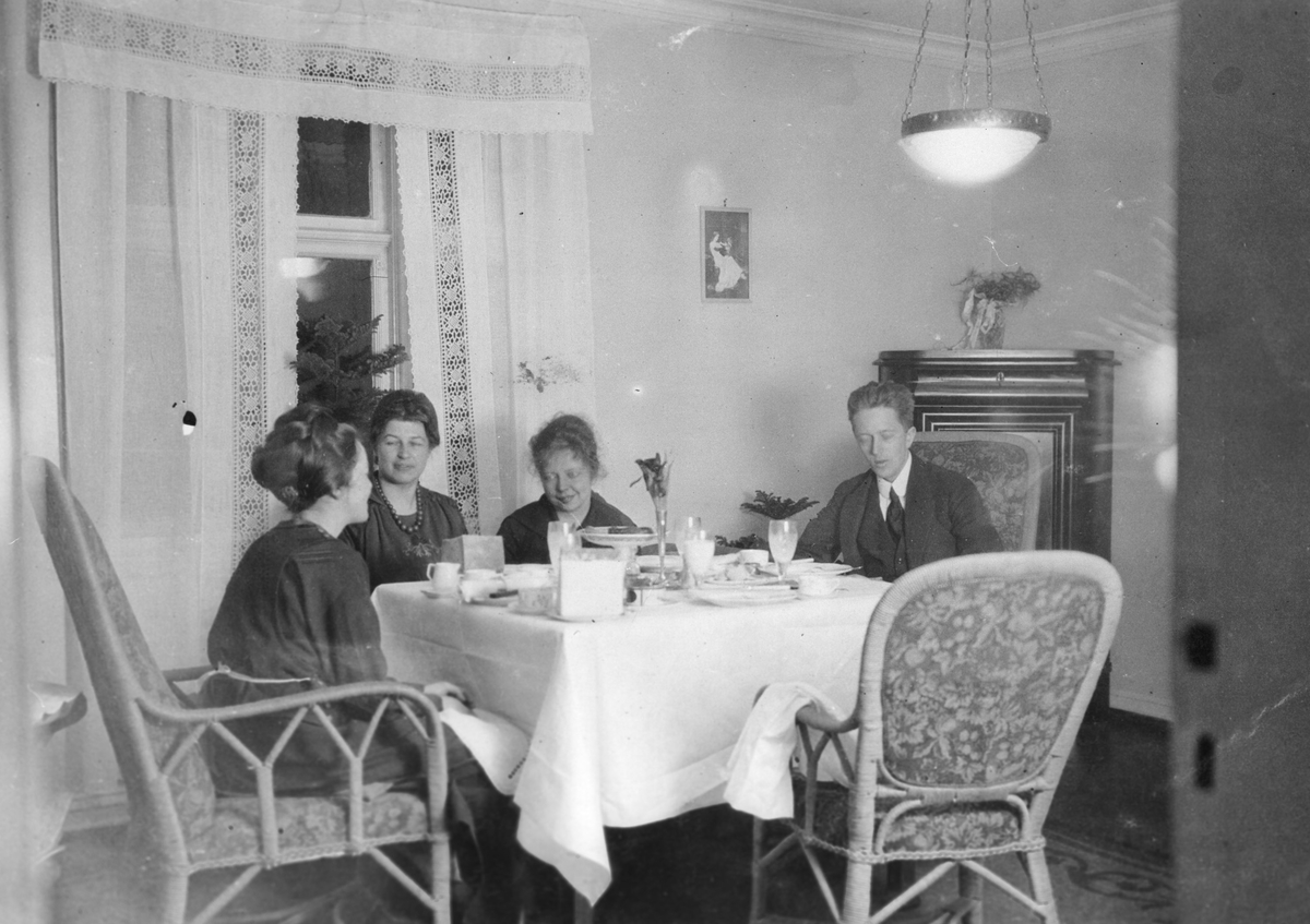Tre kvinner, en mann, oppdekket bord, hjørneskap, interiør stue