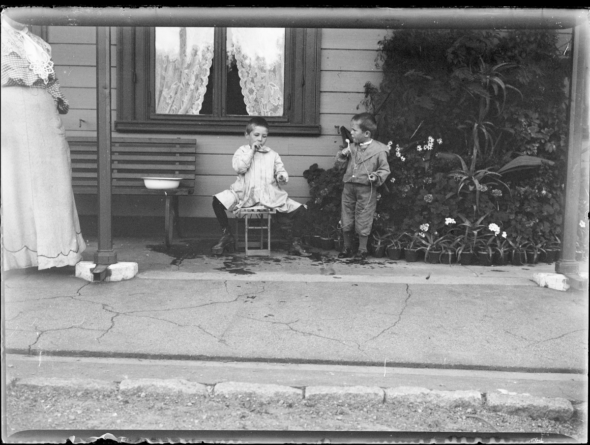 To av Christian Pierre mathiesen sine gutter foran et hus blåser såpebobler med pipe.