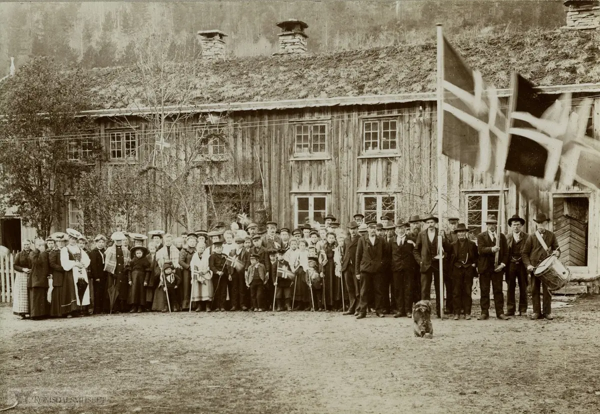 17 mai i Austigard, Sæterbø, Bæverdalen., Huset ble revet i 1981...Frå venstre: Synnøve Sæterbø (Holtå), Ann Svorken, Johanna Bæverfjord, Oline Gaasvik(Austistu Holten), Magnhild Gaasvik (Austistu Holten), Ingeborg Gravvold, Eli Holten,g.Sæterbø, Lisbeth Sjømæling, Johanna Holten (delvis skjult), Brit Svorken. Bak henne: Marit Haugen, Tomine Bæverfjord. Bak henne: Guro Bele, Gunhild Sæterbø, g.Bævre (Nyhusa) med sonen Hans Bævre framom seg...Ingeborg Sæterbø, Randi Holten,g. Berset. Mellom dei bak: Eli Bæverfjord. Vidare i 1.rekkje med kvitt sjal og flagg: Ellen Sæterbø (Utistu`n). Bak henne med hatt: Ingeborg Aasgaard. Sivert Sæterbø(med flagg), bak han: Sigrid Sæterbø,g.Holten(med hatt). Heilt bak framom døra: Edvard Sæterbø(Borstu`n) med son Hans Sæterbø på armen. Framom han med kvit bluse: Johanna Sæterbø, g.Holten, framom henne til høgre: NN, bakom henne: Gjertrud Sæterbø (delvis skjult) med dotter Ingeborg Sæterbø på armen...(Tekst Kjelde: Johanna Holten, Toresæter (f. Sæterbø i 1890), ca. 1980.) (Tekst: Tor Holten)..