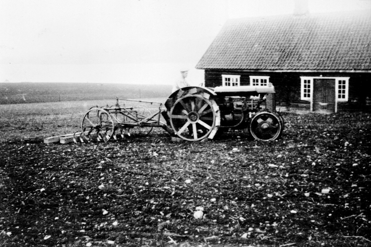 Våronn på Øvre Sund, Helgøya. Otto Sund (1884-1963) med jerntraktor av merke Fordson og exellent kultivatorharv på jordet ved Østre Sund. Hovedbygningen på Østre Sund i bakgrunn.