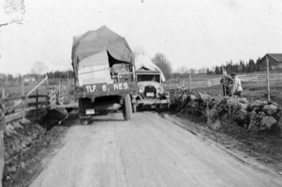To biler møtes på smal bygdeveg. Til venstre med flyttelass er Chevrolet 1934 modell tilhørende Hoel gård, Nes, Hedmark med Emil Søberg som sjåfør. Til høyre er en Ford AA modell 1928-29.