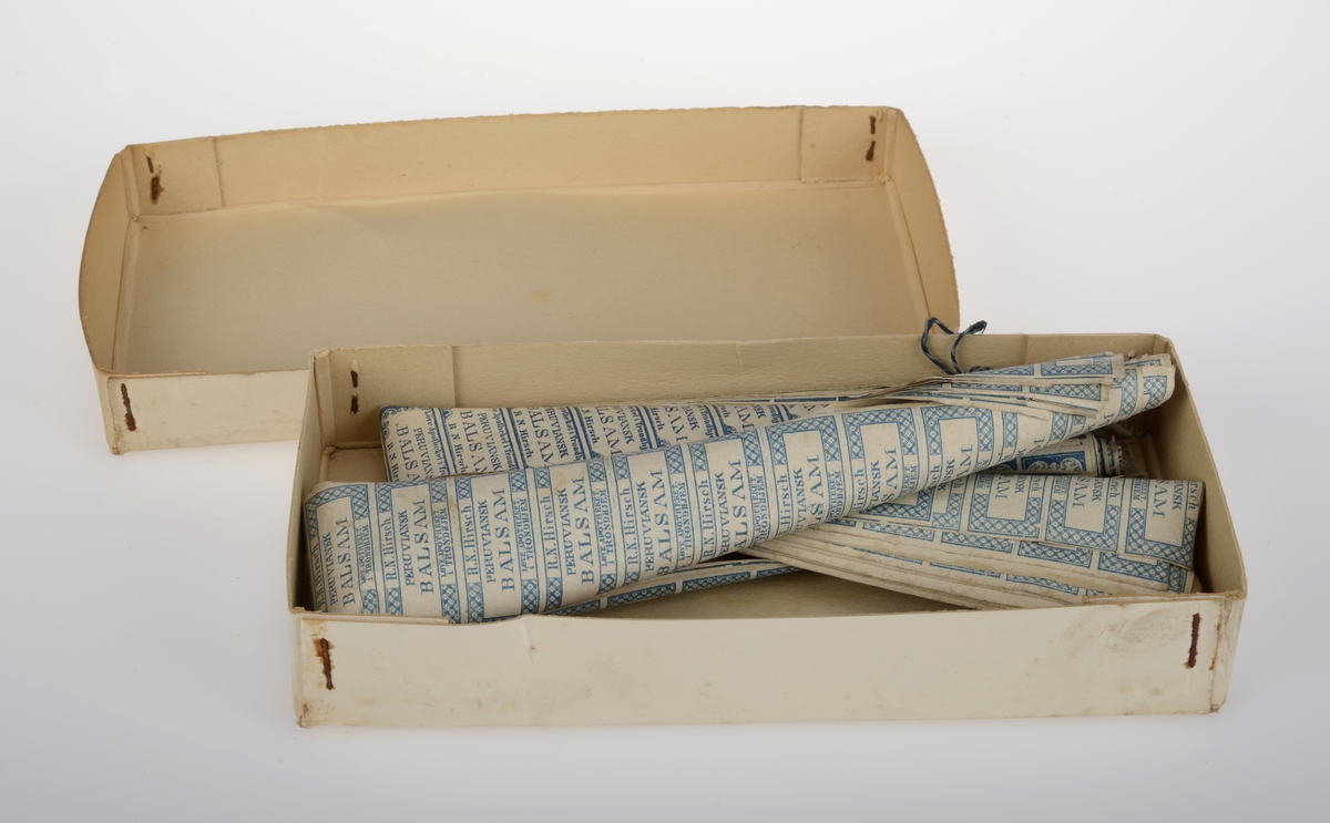 Rektangulær eske av papp med lokk inneholdene noen hundre trykte etiketter av papir.