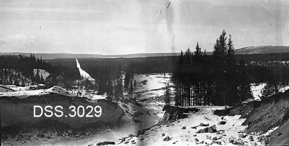 Osfallet i Søndre Osa.  Bildet er tatt etter storflommen i 1916 og viser hvordan elva har gravd seg gjennom og djupt ned i ei sandegg.  Våningshus og nåleskog i bakgrunnen.  Vinteropptak. 