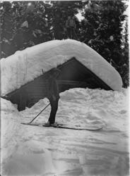 En mann på ski utenfor ei tømmerkoie i skogen.