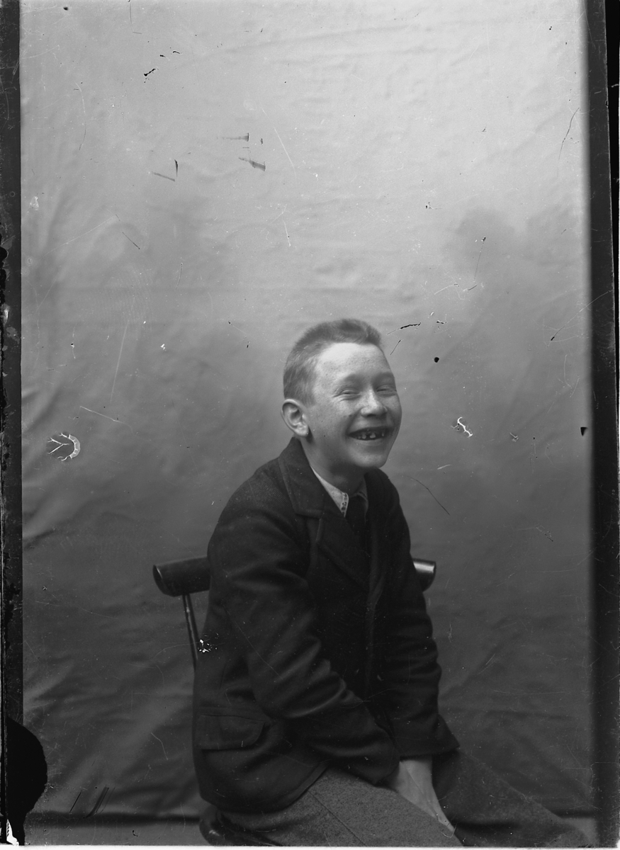 Portrett, leende gutt på stol i studio. Ukjent. 