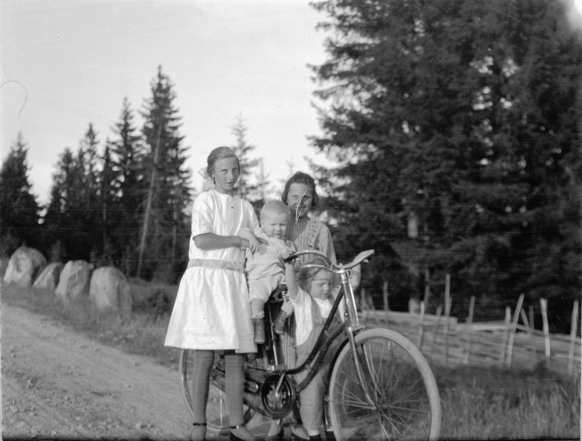 To jenter og et barn ved en sykkel på en landevei i skogen. 