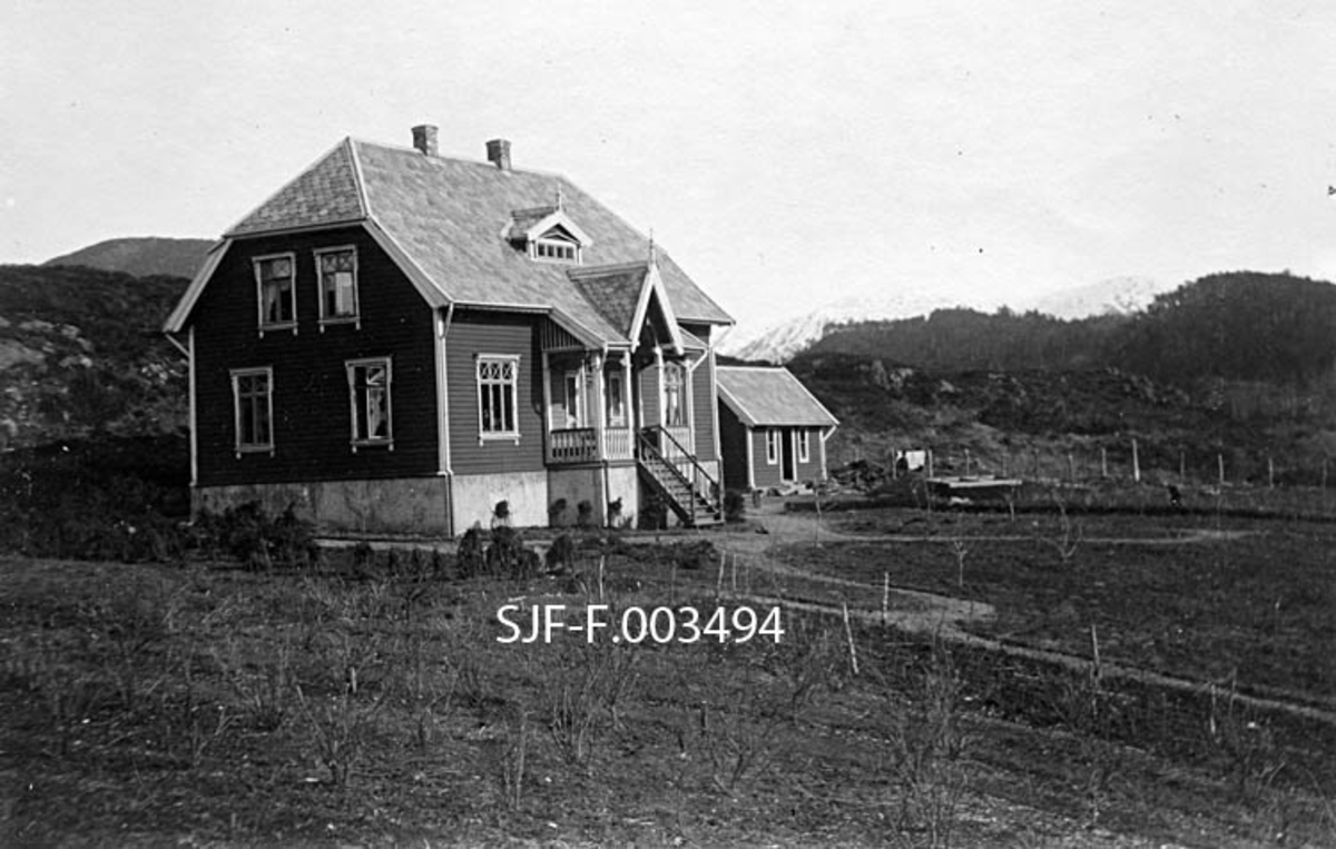 Bygning på Bergens Skogselskabs planteskole på Ekhaug i Os (Syfteland) i Hordaland, fotografert i 1904.  Bygningen, som har et staselig villapreg, var antakelig ny på dette tidspunktet.  Det er rimelig å anta at den inneholdt kontorer og boligrom for familien til planteskolebestyreren (Hans Marthinsen Skinstad [1878-1956]).  Huset sto på en forholdsvis høg, støpt mur.  Det hadde liggende utvendig panel som var malt i en forholdsvis mørk farge, mens vindusomramminger, vindskier og hjørnebord var kvitalte.  Midt på langveggen var det en veranda med ornamentert rekkverk og med trapp ned mot den nedenforliggende planteskolen.  Huset hadde halvvalmet tak som var tekket med lappskifer og hadde to skorsteinspiper.  Sentralt på ei av takflatene, rett over den nevnte verandaen, var det en liten ark med vinduer, som sikkert kastet lys inn i det øvre etasjeplanet.  Bakenfor den beskrevne bygningen, litt til høyre, skimtes en mindre uthusbygning, utført i samme typer materialer og med samme fargesetting som hovedhuset, men som var mindre og enklere i formen.  Foran de nevnte bygningene var det et felt med bladløse småtrær.  Dette kan være bærbusker, som også inngikk i produksjonen på Ekhaug i denne perioden.  I bakgrunnen skimtes et utmarkslandskap med forholdsvis nakne bergkoller og (aller bakerst) fjell med snødekte topper. 