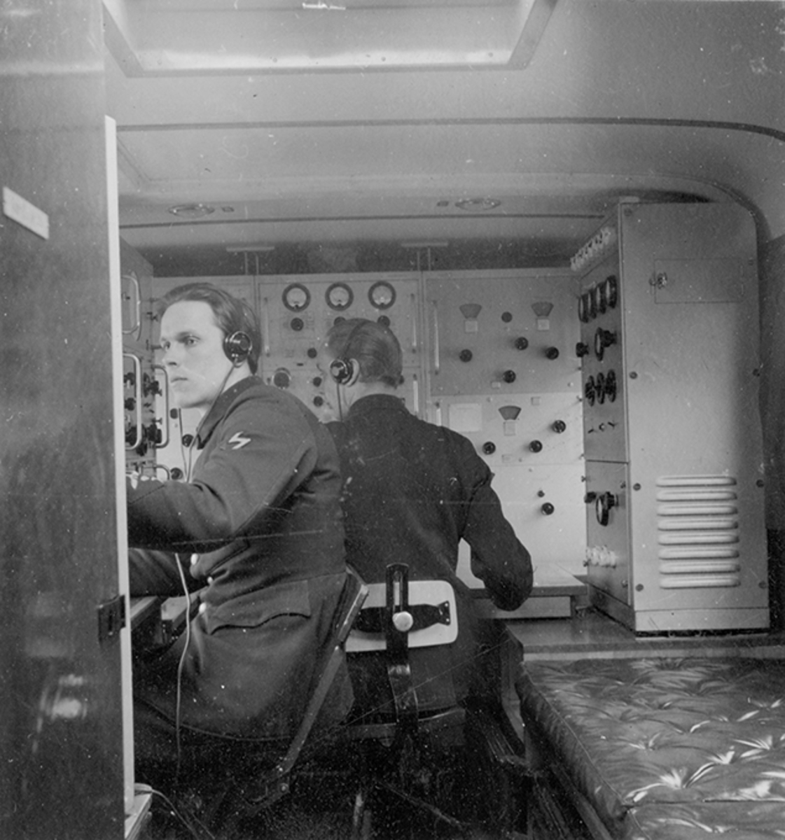 Två män i arbete i radiobuss, transportabel markradiostation modell 9. Interiör.