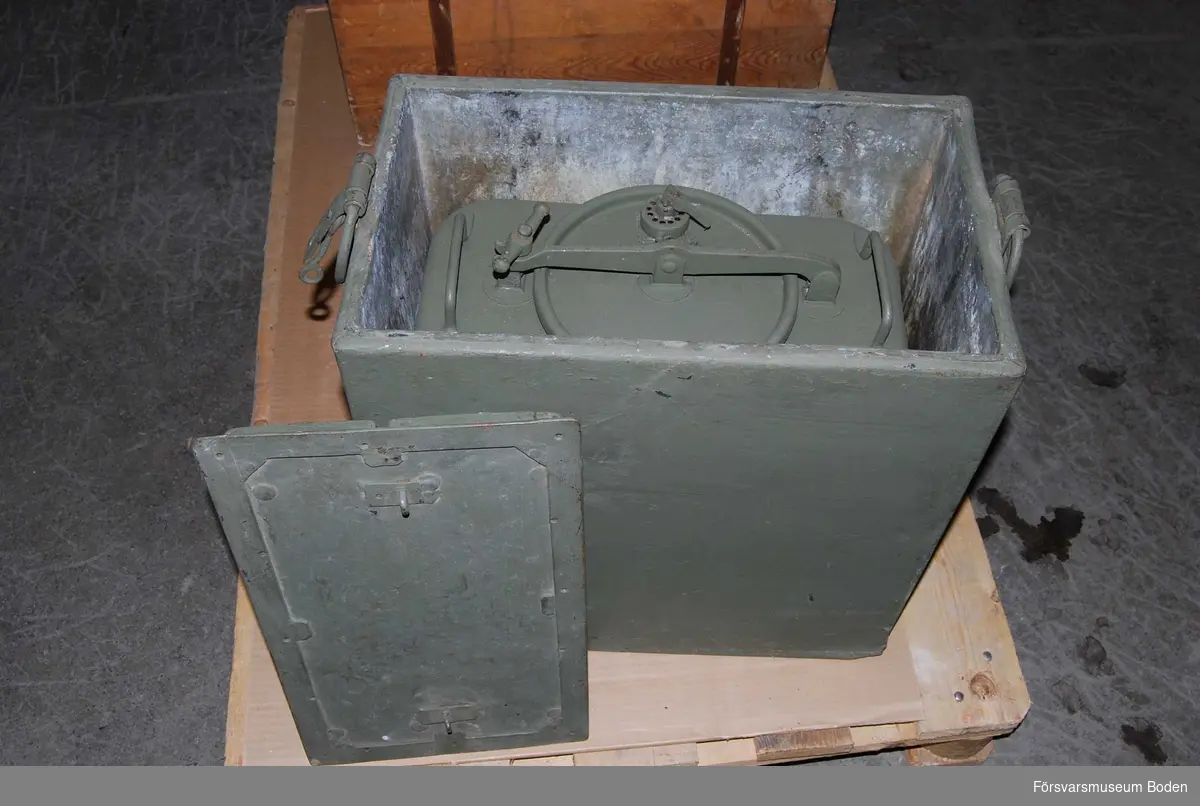 Låda av plåt med isolerade väggar och lock. Inuti är en kokkittel placerad samt ett ställ för kitteln. Kittelns lock låses med hävarm och låsvred.