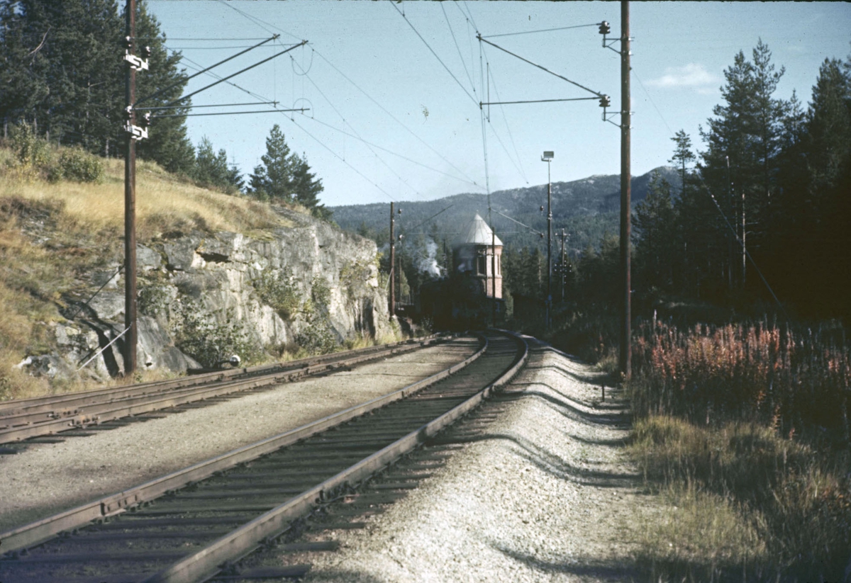 To damplokomotiver type 31b med tog retning Bergen passerer vanntårnet på Austvoll stasjon