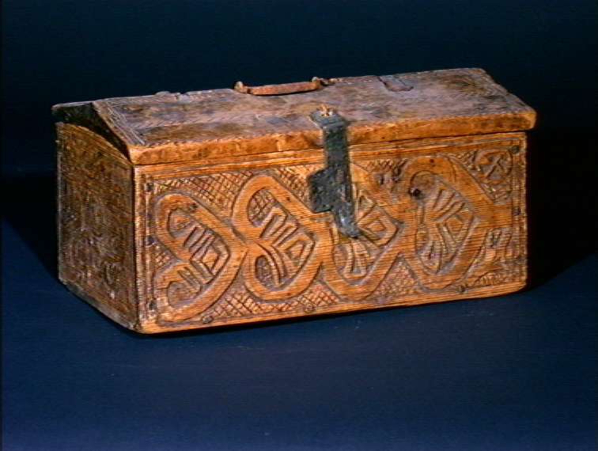 Skrin med flate sider of lett takformet lokk. Hengslet i bakkant og låsmekanisme i forkant. Håndtak midt på lokket. Hele utsidenhar skurd dekor med ranker, dyr og mennesker.