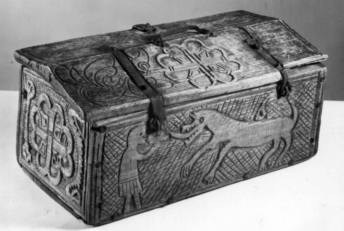 Skrin med flate sider of lett takformet lokk. Hengslet i bakkant og låsmekanisme i forkant. Håndtak midt på lokket. Hele utsidenhar skurd dekor med ranker, dyr og mennesker.