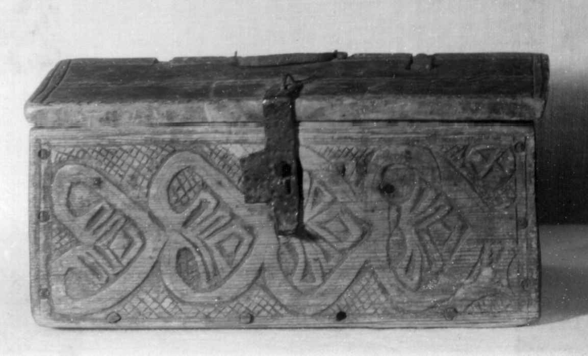 Skrin med flate sider of lett takformet lokk. Hengslet i bakkant og låsmekanisme i forkant. Håndtak midt på lokket. Hele utsidenhar skurd dekor med ranker, dyr og mennesker.