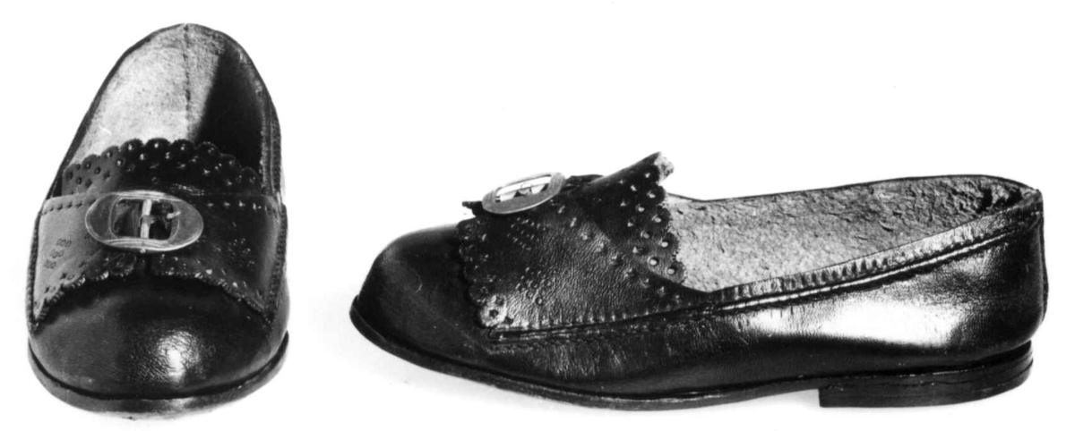 Svart sko med metall spenne og preget mønster