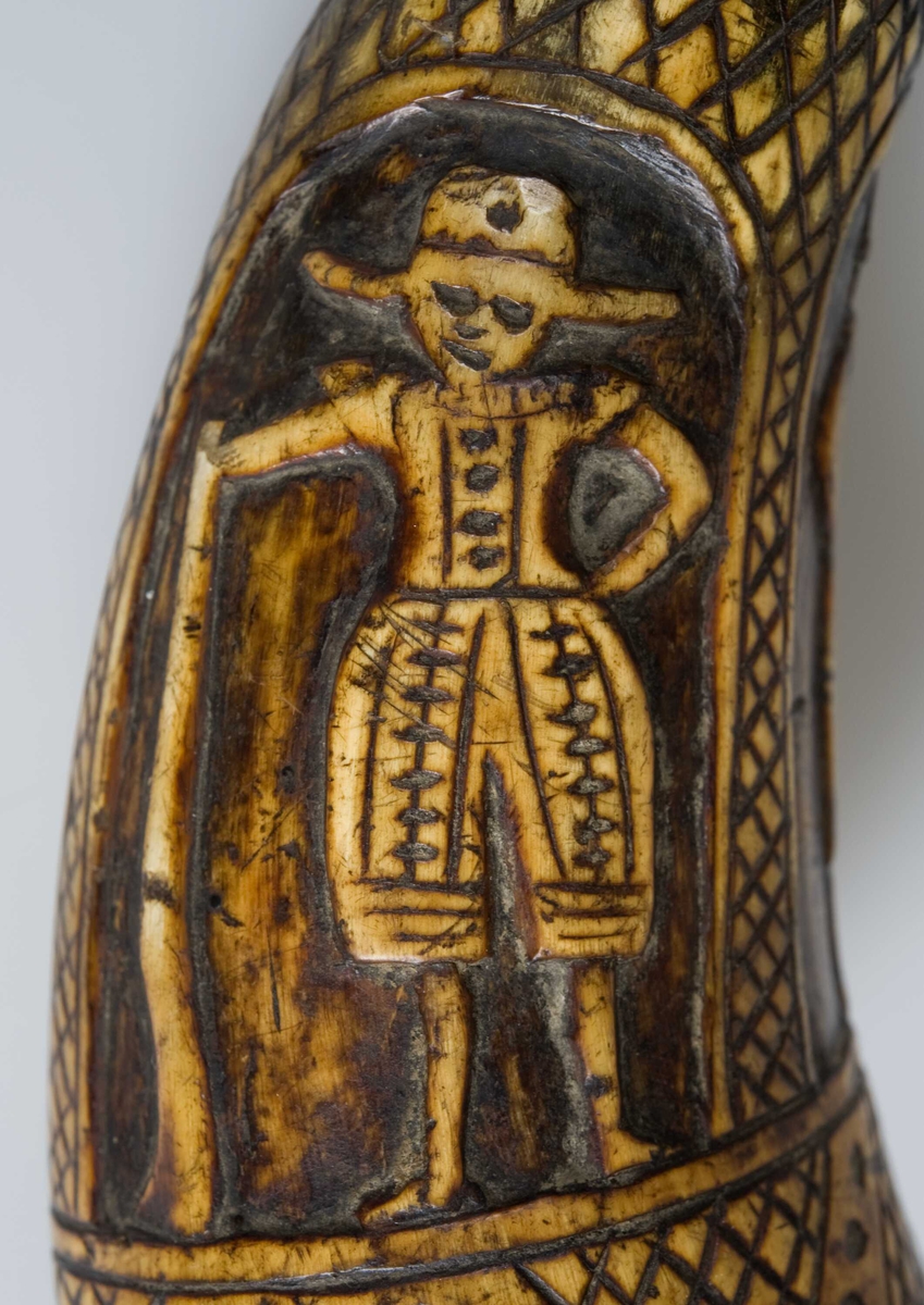 Krutthorn med figurer utskåret i relieff. Endestykket i jern har nøkler for å spenne geværlåsens hane.
