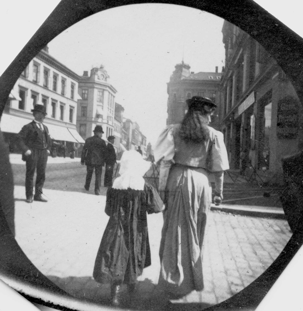Frk.Martha Arneberg og ei lita jente spaserer langs Karl Johan, Oslo  med ryggen til fotografen i retning mot Egertorget. 