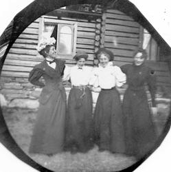 Golå, Sør-Fron, Oppland. Fire kvinner arm i arm foran tømmer