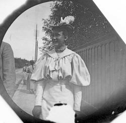 Frk. Solveig Berg langs en  vei med gjerde. Skog i bakgrunne